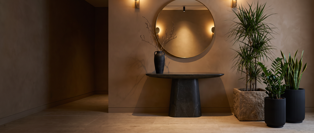 Entrée design avec console en pierre, vase noir, bac minéral et cache-pots noirs garnis de plantes artificielles